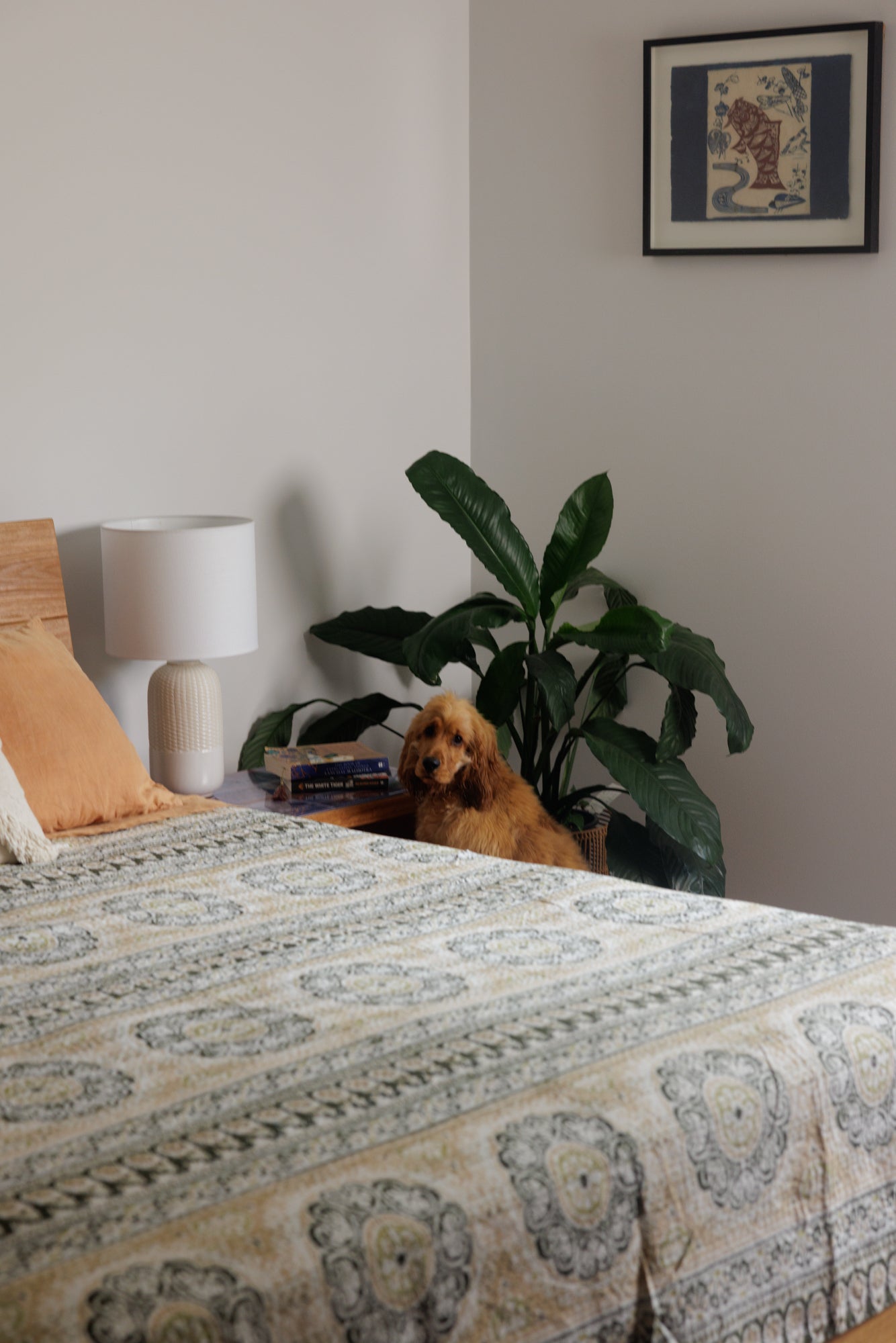 A Kantha quilt with a floral pattern draped over the edge of a bed, displaying a blend of colors including beige, brown, and green.